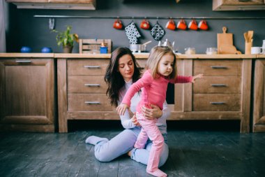 Sevimli genç bayan mutfakta komik kızıyla oynuyor. Güzel bir annenin portresi kucağında taşıdığı ve küçük dişi çocuğunu izlediği. Mutlu aile içinde yaşam tarzı portresi.