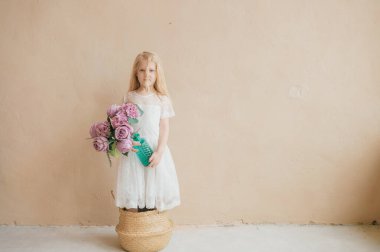 Sarı arka planda saman sepetinde duran beyaz elbiseli güzel, uzun saçlı kız çocuğu. Elinde bir buket çiçekle elinde vazo tutan güzel bir kadının ev yapımı portresi.