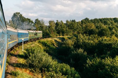 Yazın trenle gezmekten pencere dışındaki manzara. Tepeler, dağlar ve ormanlar. Tatil ve seyahat konsepti. Tren vagonlu lokomotif tren yolu boyunca ilerliyor.