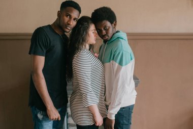 Çok kültürlü aşk ve ilişkiler kavramı. Genç beyaz kadın iki koyu tenli Afrikalı adamın arasında duruyor. Irklar arası aşk üçlüsünün kapalı bir portresi. İki Afrikalı erkek, sevgililerine sarılıyor.