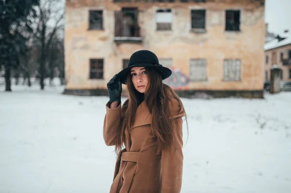身穿棕色外套 头戴黑色帽子的年轻时尚女孩站在室外 面对着被拆除的房子 — 图库照片