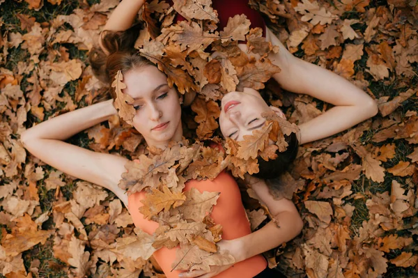 Две Молодые Девушки Покрытые Осенними Листьями Лежат Земле Смотрят Разные — стоковое фото