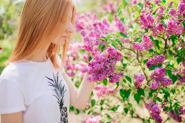 赤い髪をした美しい若い白人女性は花とライラックの庭で背を向けて — ストック写真