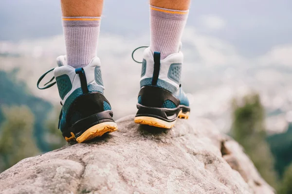 Mood photo of male legs wearing sportive hiking shoes with strong protective sole. Mens legs in trekking footwear for mountain travel standing on stone outdoor at nature on abstract background