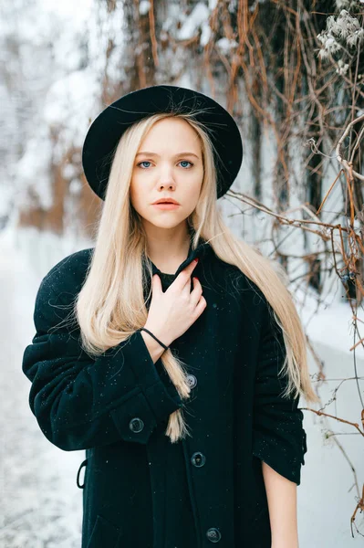 身穿黑色衣服头戴黑色帽子的时髦漂亮金发姑娘站在街上篱笆边 — 图库照片