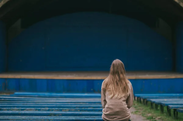一个孤零零的女孩坐在露天剧场的长椅上 背对着一排排的针尖长椅和场景 — 图库照片