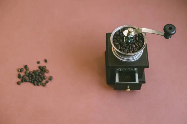 Top down vintage and mood atmospheric photo of handful of coffee beans lying together with manual wooden coffee grinder in retro style on brown textured background