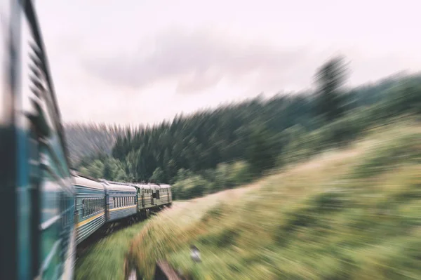 Landscape beautiful view out of window from riding train among summer nature with hills, mountains and forest. Vacation and travel concept. Locomotive with train cars moving along railroad track