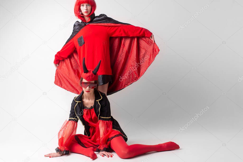 Two sexy girls dressed in halloween costumes posing in studio obver white background.