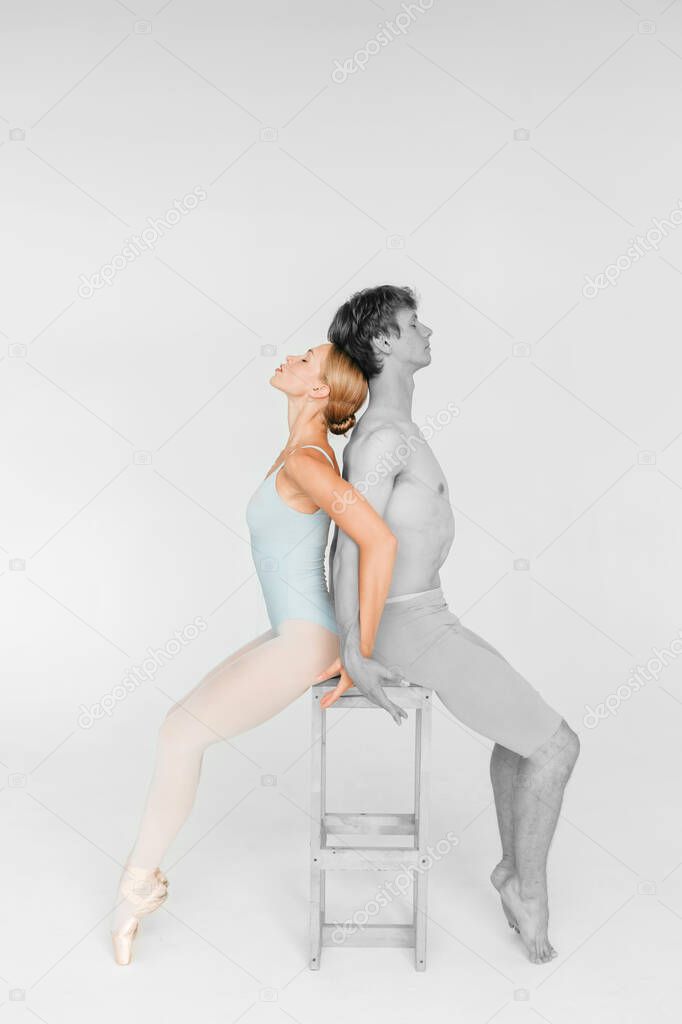 Couple of young and athletic ballet dancers sitting on chair back to back over white studio background