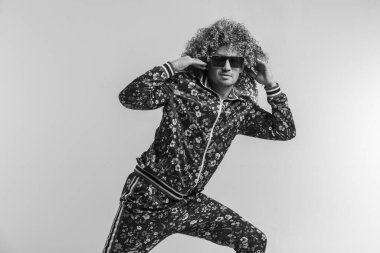 Beyaz stüdyo arka planında poz veren şık, klasik elbiseli, heyecanlı bir yetişkin komik adam. 80 'lerin modası. Eşofmanlı ve güneş gözlüklü tuhaf adam. Kapalı alanda alışılmadık bir portre. Bağıran neşeli erkek.