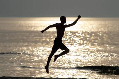Karanlık siluet, arka planda güneş ışığı olan denizdeki süper kahraman gibi elleri ayrık atlayan bir adam. Yaz akşamları denizin ötesinde dans eden tanınmaz bir adam. Özgürlük ve mutluluk kavramı