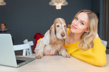 Mutlu sarışın kadın, komik cocker köpeğini kucaklar ve dizüstü bilgisayarında kameraya poz verir..
