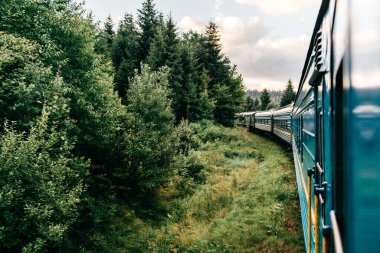 Yazın trenle gezmekten pencere dışındaki manzara. Tepeler, dağlar ve ormanlar. Tatil ve seyahat konsepti. Tren vagonlu lokomotif tren yolu boyunca ilerliyor.