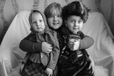 Güzel bir kızın portresi ayı kostümü giymiş küçük erkek kardeşine ve Rus tarzı şenlik elbisesi giymiş komik kız kardeşine sarılıyor. Mutlu çocukluk.