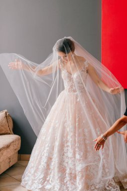 Gri arka planda, elinde çiçekle poz veren beyaz elbiseli güzel gelinin portresi.