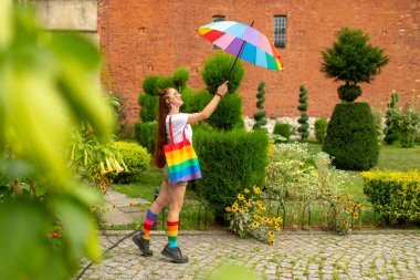 Yüzünde Igbt bayrağı olan, elinde gökkuşağı şemsiyesi olan ve renkli çoraplar giyen neşeli bir lezbiyen. Igbt çantalı biseksüel kız mutlu yüzle poz veriyor.