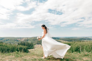 Beyaz gelinlikli güzel gelin doğada bir tepede poz veriyor.
