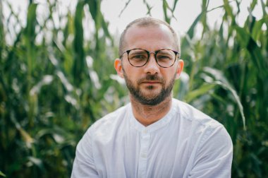 Kısa saçlı, siyah tüylü, gözlüklü ve beyaz gömlekli yakışıklı bir adamın portresi..