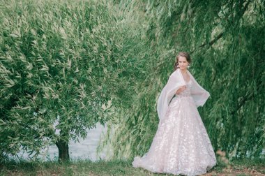 Beyaz gelinlik içinde güzel bir gelin elinde çiçeklerle dışarıda poz veriyor..