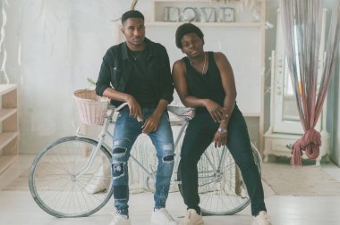 İki mutlu yetişkin Afrikalı erkek, dekoratif stüdyoda bisikletin yanında durup kameraya poz veriyor. İki Afro-Amerikan erkek kapalı mekan yaşam tarzı vintage tarzı portre