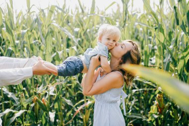 Açık mavi elbiseli genç, beyaz gömlekli, kısa siyah saçlı, beyaz pantolonlu, güçlü beyaz saçlı, yaz aylarında mısır tarlasında sarışın oğluyla oynayan güzel bir anne..