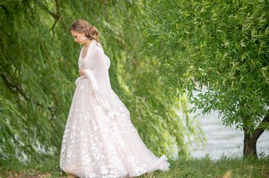 Beyaz gelinlik içinde güzel bir gelin elinde çiçeklerle dışarıda poz veriyor..