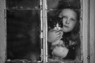 Küçük komik kızın portresi ve sevimli kedisi köy evindeki eski pencereden dışarı bakıyor..