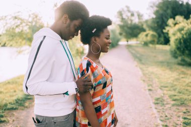 Gülümseyen yüzlü güzel Afro-Amerikan çifti sonbahar parkında gün batımında kucaklaşır.