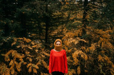 Kırmızı ceketli, siyah pantolonlu çekici bir kadın soğuk sonbahar ormanlarında ısınmak için kafasına atkı takmış..