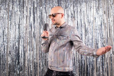 90 'ların şarkıcısı, gümüş gömlekli ve deri pantolonlu, stüdyoda şarkılar söylüyor.