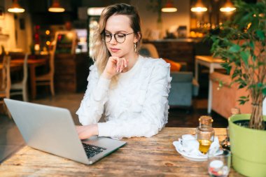 Kafe masasında dizüstü bilgisayar kullanan genç ve güzel bir kadın. Mutlu gülümseyen kız internette çalışıyor ya da defter kullanırken öğreniyor. Serbest çalışma, iş adamları konsepti.