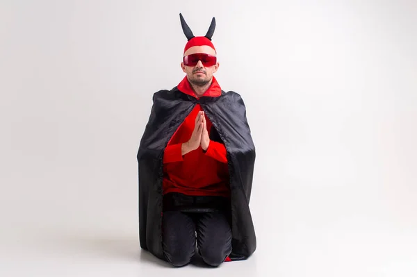 Strange man in devilish costume and red hat with black horns posing over white background.