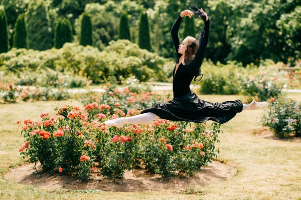 Jovem Bailarina Vestido Preto Saltando Entre Arbustos Rosa Parque — Fotografia de Stock