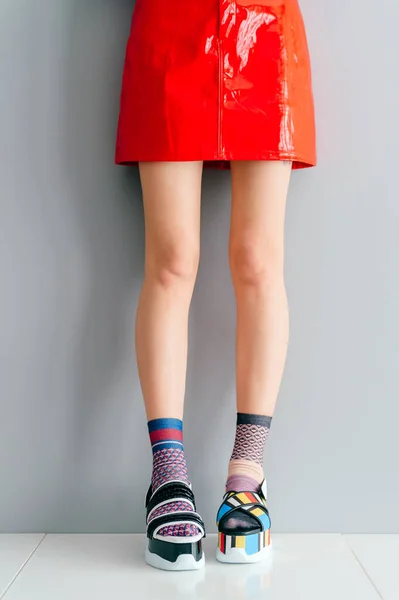 一双漂亮的女腿穿着不相配的时髦袜子站在两个不同的时尚的高楔形皮鞋白色表面 穿着红色短裙穿着高跟鞋的奇怪的小女孩 — 图库照片