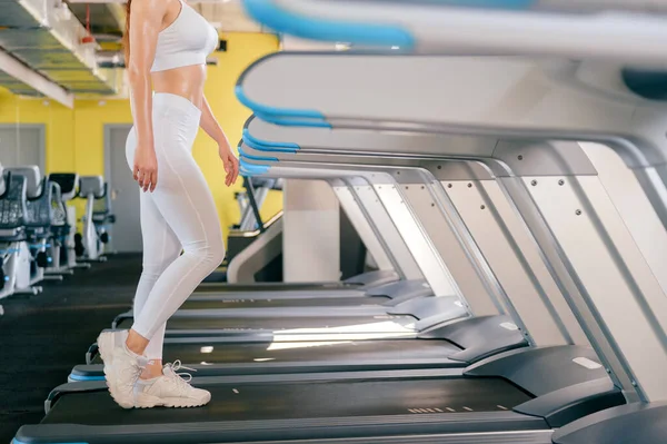 young sport woman running on treadmill in gym, keeps fit, burn calories on running machine, wearing white sportswear and sneakers