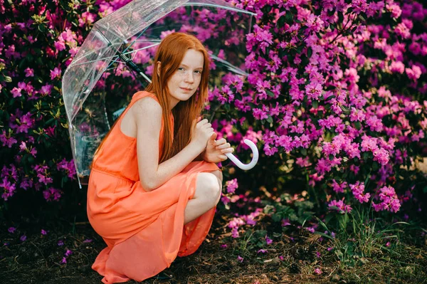 長い赤い髪をした奇妙な若い女の子 夏のオレンジのドレスでかなり顔は庭で傘を保持しています — ストック写真