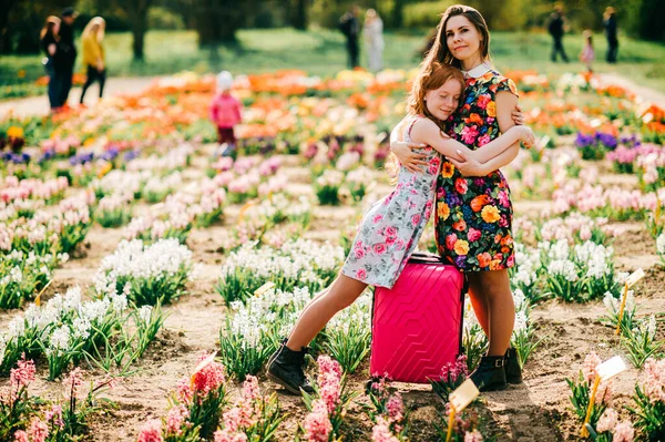 Attractive child with long red hair rejoices with her pretty tall sister relaxes and rejoices in the big flower garden at the weekends.