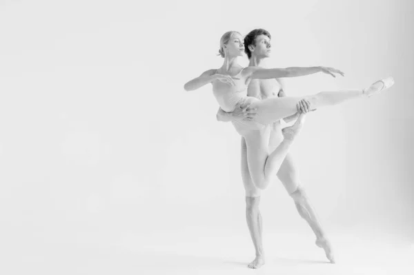 Young couple of modern ballet dancers posing over white studio background