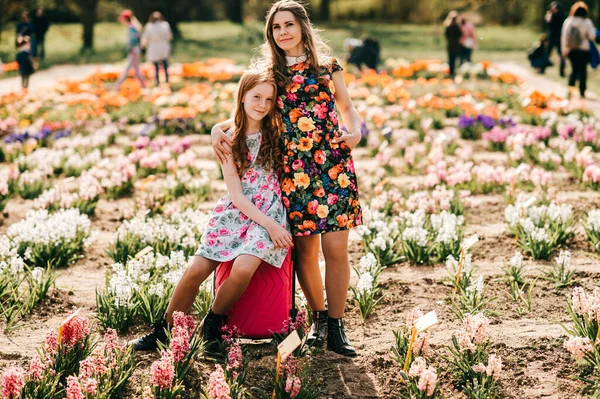Attractive child with long red hair rejoices with her pretty tall sister relaxes and rejoices in the big flower garden at the weekends.