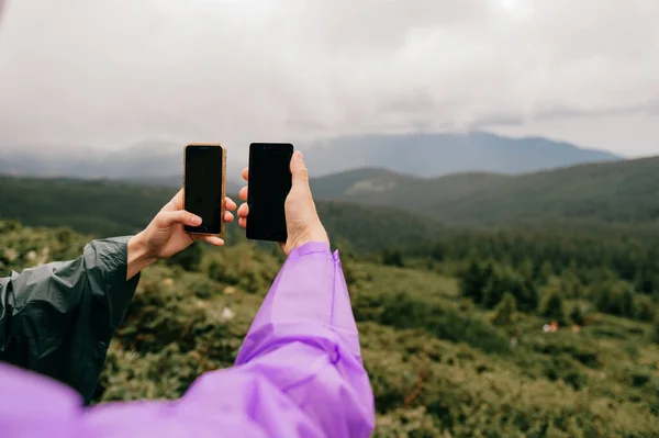 Unrecognizable travelers hands with smartphones take picture of fabulous nature landscape view in summer rainy day. Unknown tourists in camping adventure take selfie with cellphones. Happy moments