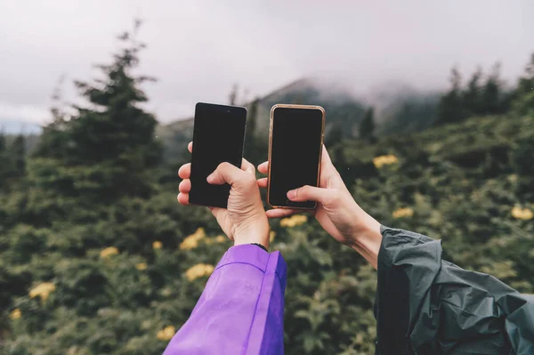 Goverla, Ukraine - July 14, 2018: travelers hands with smartphones take picture of nature landscape view in summer rainy day. Ttourists in camping adventure take selfie with cellphones. Happy moments