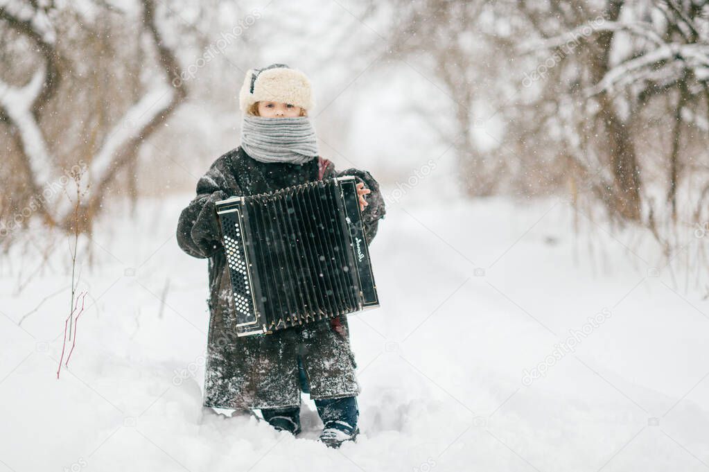 Caucasian cheerful girl in oversized warm padded jacket standing on snowy road in winter day with accordion