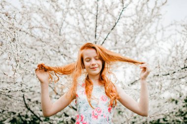 Beyaz elbiseli, kızıl saçlı harika bir kızın büyük bahar bahçesinde eğlenirken çekilmiş fotoğrafı..