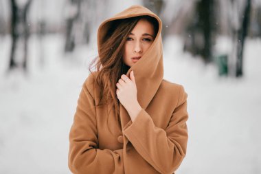 Gürcü görünümlü güzel, uzun saçlı esmer kız portresi kış parkında kahverengi ceketle poz veriyor.