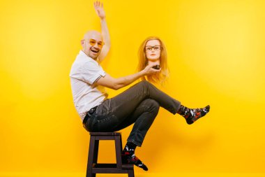 Alışılmadık kel iş adamı plastik sarışın kadınla oynuyor. Heyecanlı aptal adam. Gözlüklü şık bir adam bir kıza aşık. Sarıda izole edilmiş komik bir çift portresi. Erkek yüz ifadesi.