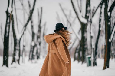 Kahverengi ceketli neşeli kız, kış ağacı vadisinde poz veriyor..