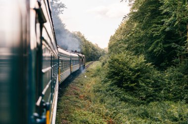 Yazın trenle gezmekten pencere dışındaki manzara. Tepeler, dağlar ve ormanlar. Tatil ve seyahat konsepti. Tren vagonlu lokomotif tren yolu boyunca ilerliyor.