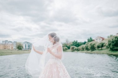 Yüzü peçeyle örtülmüş, arka planda gölle dışarıda poz veren gelinlik giymiş güzel bir gelin..