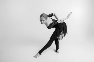 Beyaz bir stüdyo arka planında soluk tenli jimnastik egzersizi yapan çekici bir bayan jimnastikçinin siyah beyaz resmi.